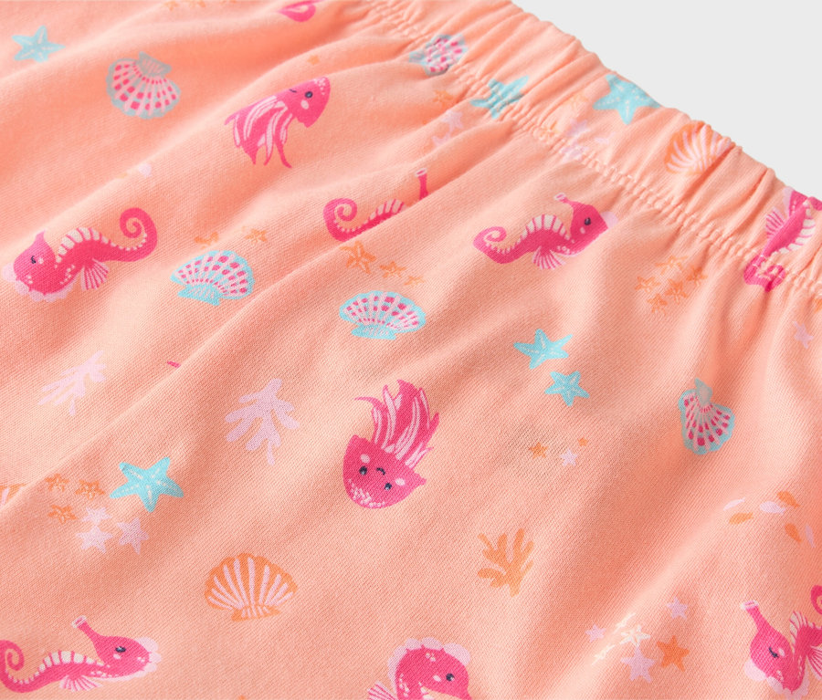 Gros plan d'un pantalon couleur pêche avec une ceinture élastique, imprimé de motifs roses d'hippocampes, de méduses et de coquillages.