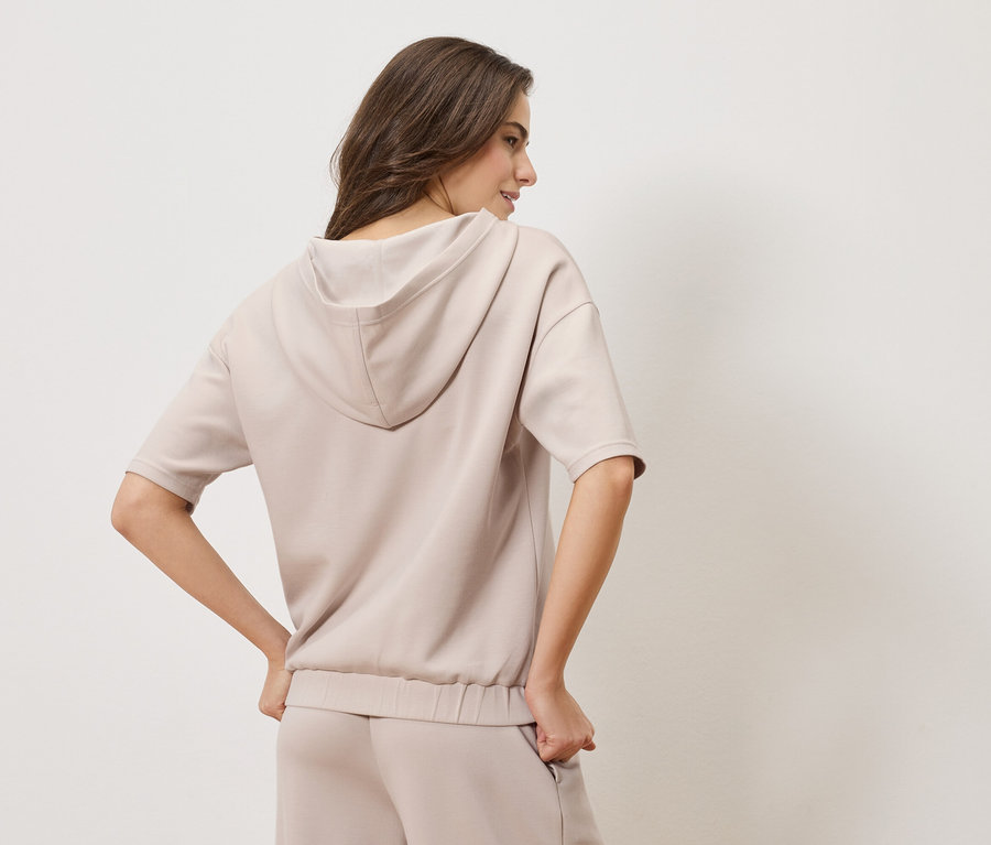 Femme vue de dos portant un sweat à capuche beige et un pantalon assorti.