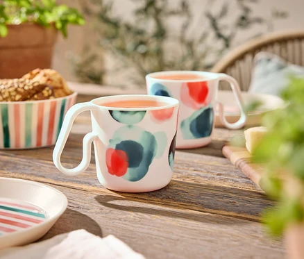 Deux tasses à motif abstrait sont posées sur une table en bois à côté d'un bol de biscuits et d'assiettes.
