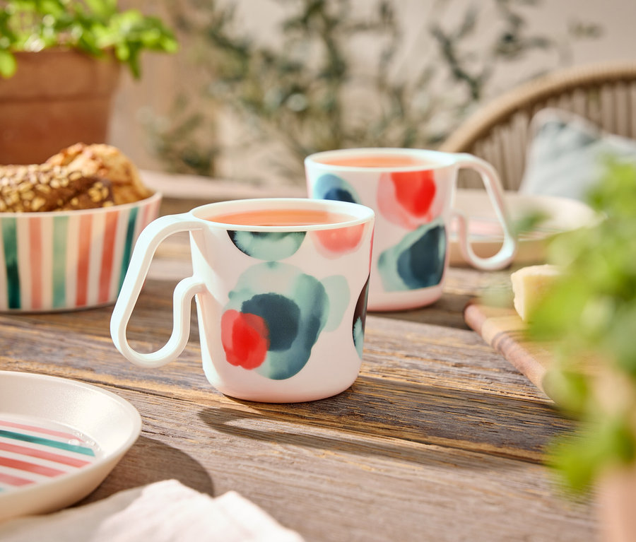 Deux tasses à motif abstrait sont posées sur une table en bois à côté d'un bol de biscuits et d'assiettes.