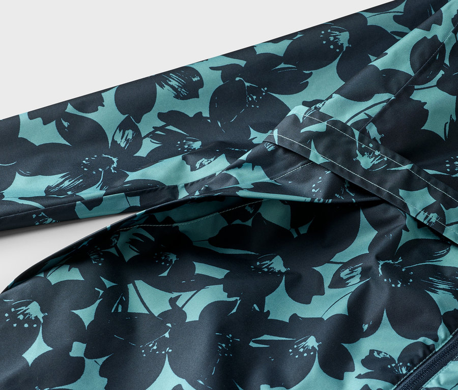 Gros plan sur une veste bleu-vert à motif floral bleu foncé, avec une manche et une fermeture éclair visibles.