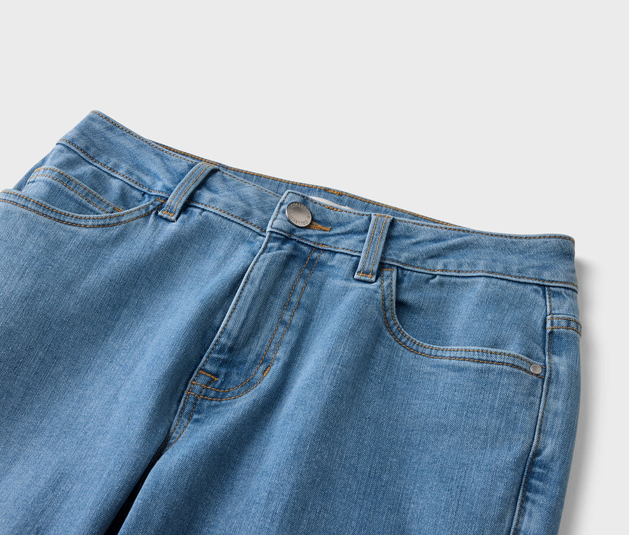 Gros plan d'un jean bleu clair avec des poches, des passants de ceinture et un bouton argenté.
