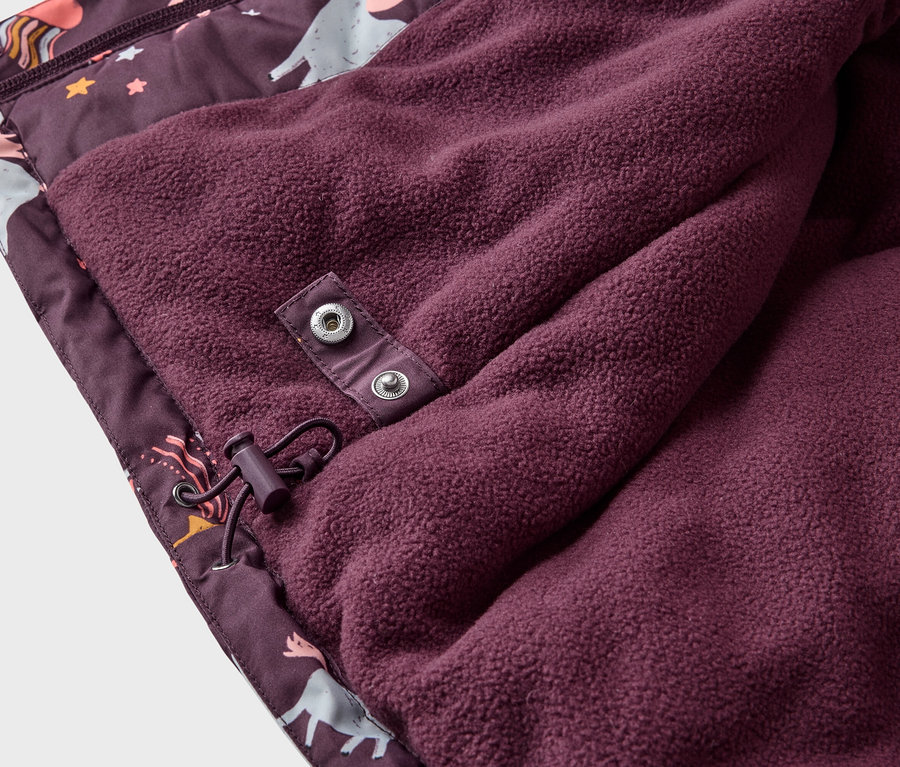Gros plan sur une veste bordeaux à motif de licorne avec une doublure en polaire, fixée par des boutons-pression et un cordon de serrage.