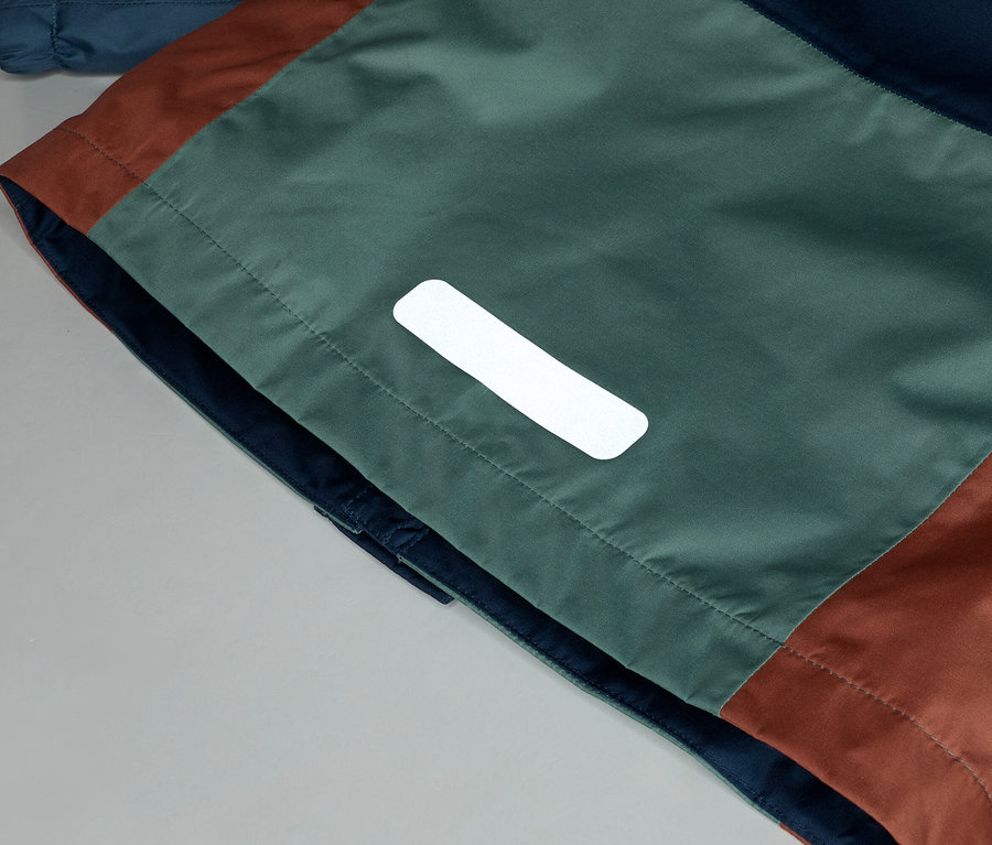 Gros plan d'une veste avec des blocs de couleurs marine, vert et marron et un détail réfléchissant.