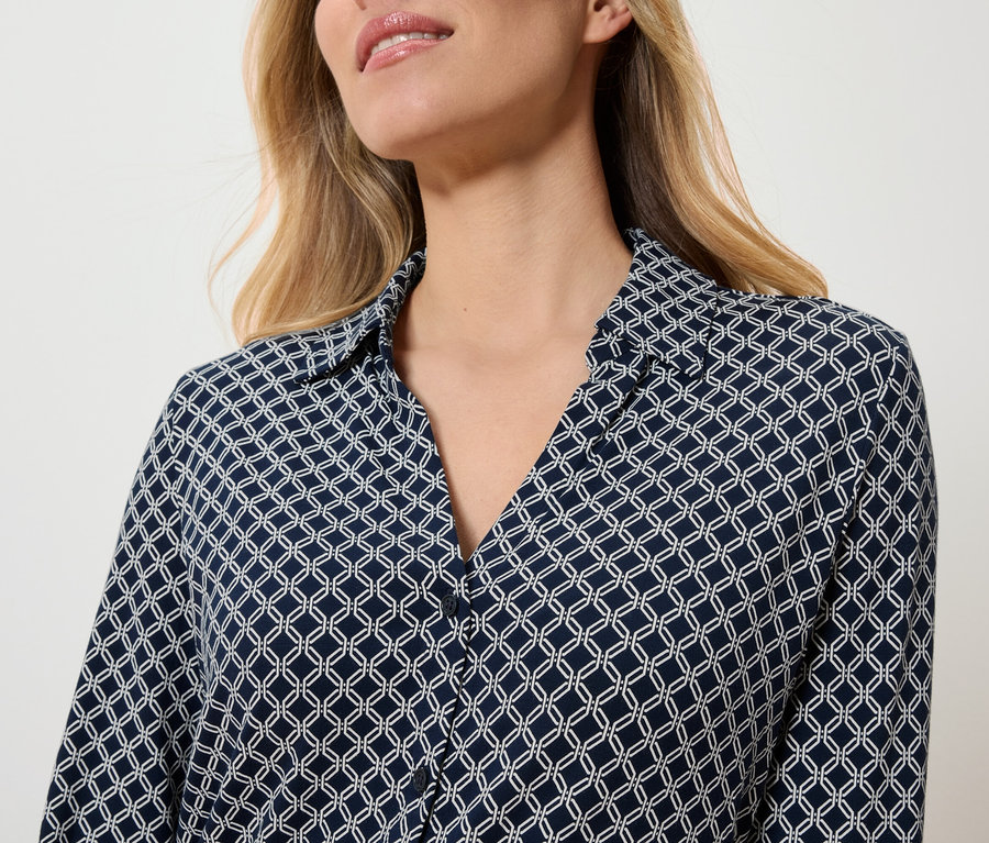 Haut du corps d'une femme portant un chemisier bleu marine avec un motif géométrique blanc.