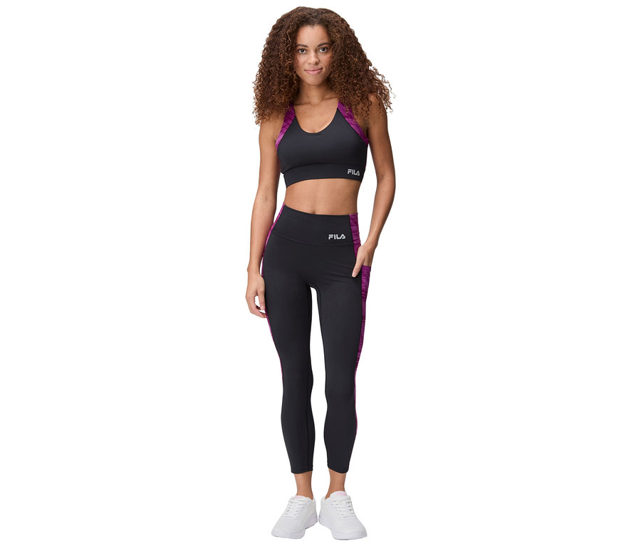 Femme debout portant un soutien-gorge de sport noir et un legging avec des accents violets et des baskets blanches.