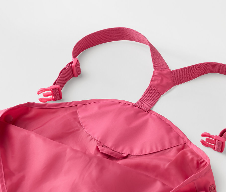 Gros plan d'un pantalon de pluie rose pour enfant avec des bretelles réglables et des boucles sur un fond blanc.