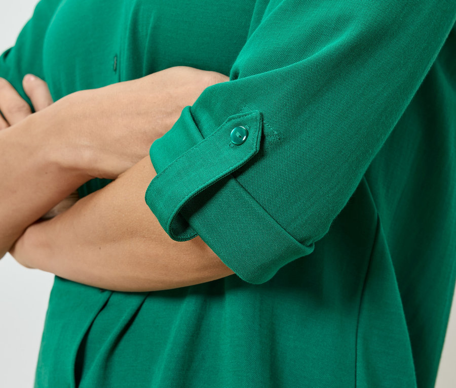 Gros plan d'une personne aux bras croisés portant une chemise verte avec des boutons et des manches retroussées.
