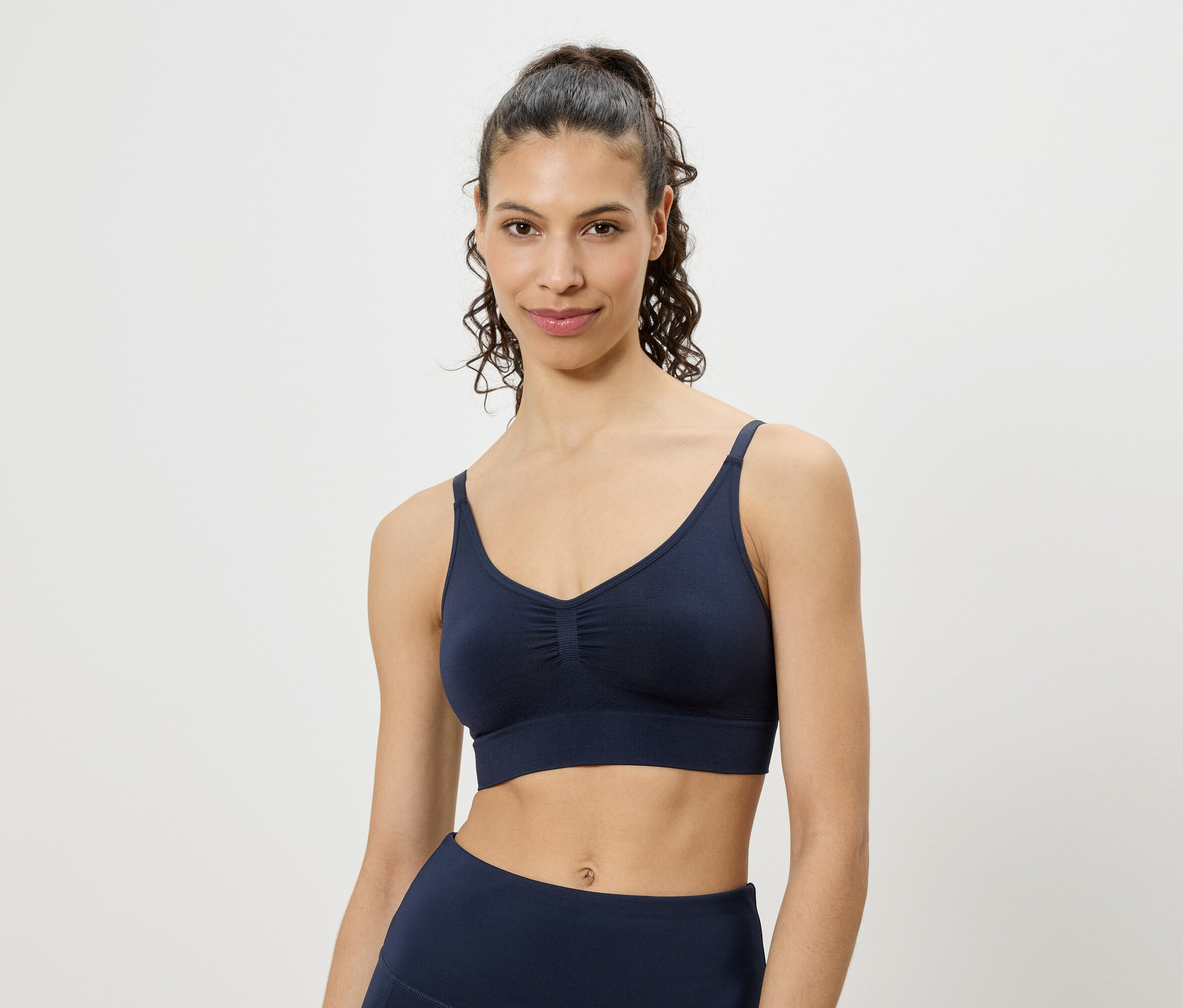 Une femme porte un soutien-gorge de sport bleu marine et un legging sur fond blanc.