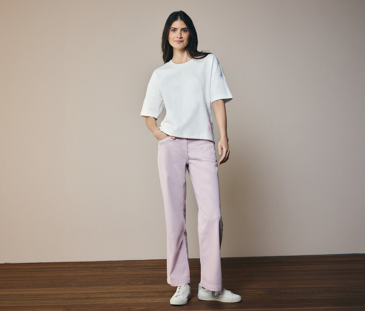 Femme portant un t-shirt blanc et un Jeans CECIL « Neele ». Elle se tient sur un plancher en bois devant un fond beige.