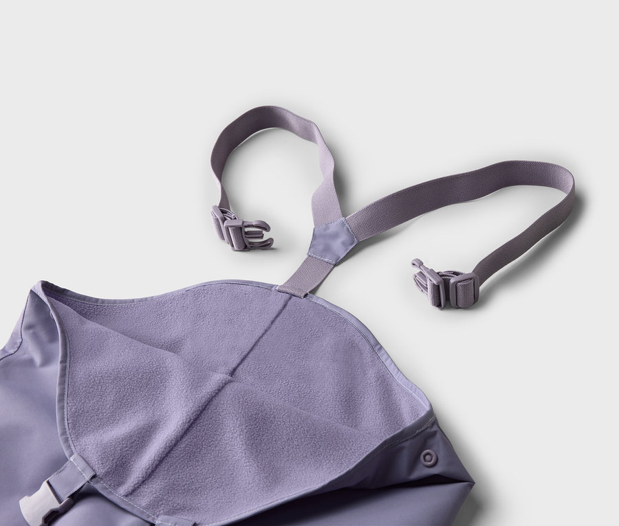 Gros plan d'un pantalon de pluie violet à bretelles avec boucles sur fond blanc.