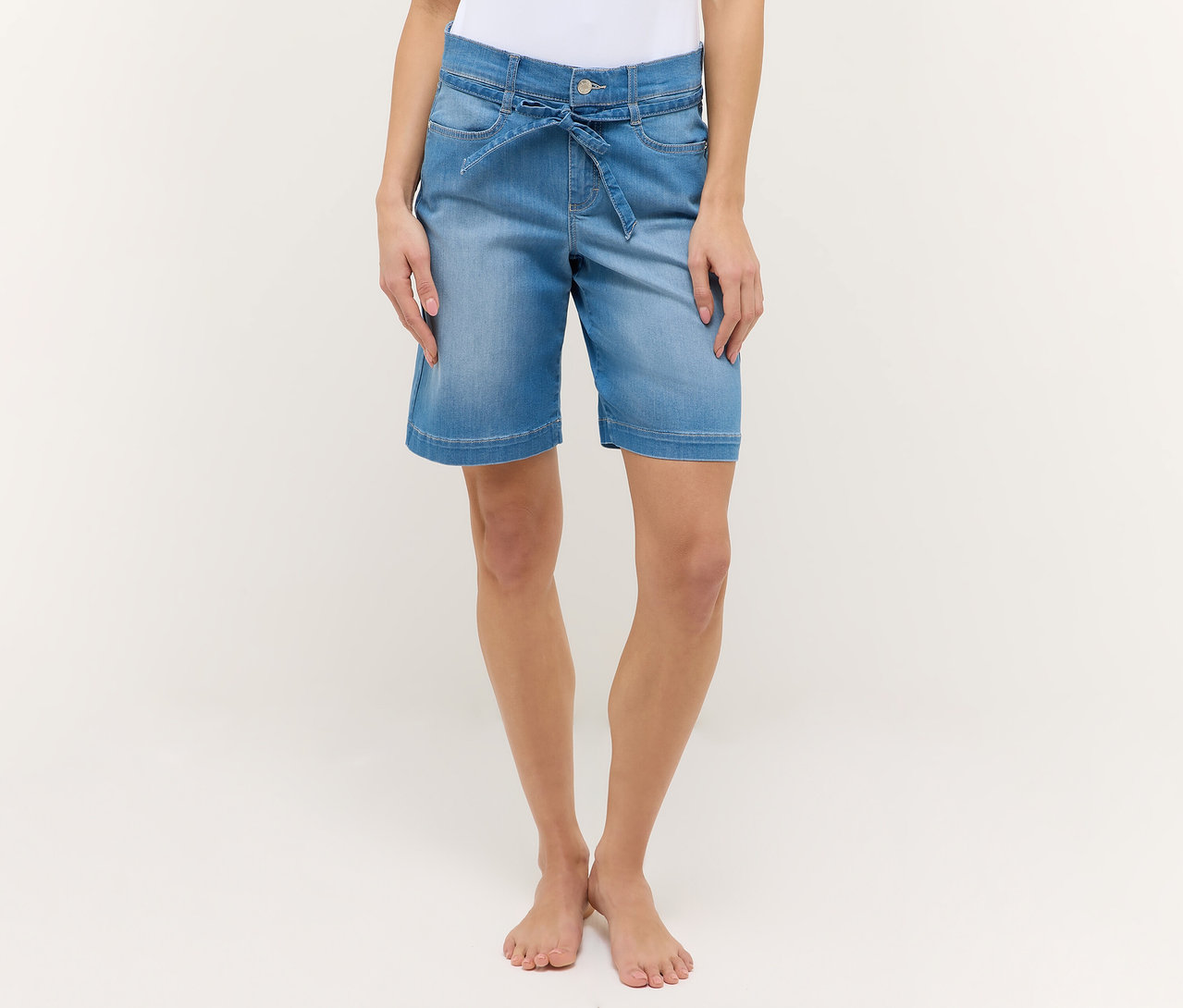 Une femme porte un short Angels Denim «
Lia City
» bleu clair avec une ceinture à nouer sur un fond blanc.