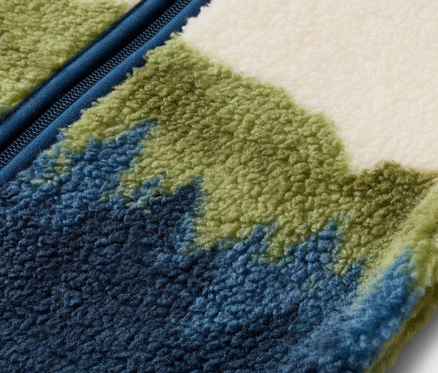 Gros plan d'une veste polaire avec une fermeture éclair bleue et un motif dans les tons de bleu, de vert et de blanc.