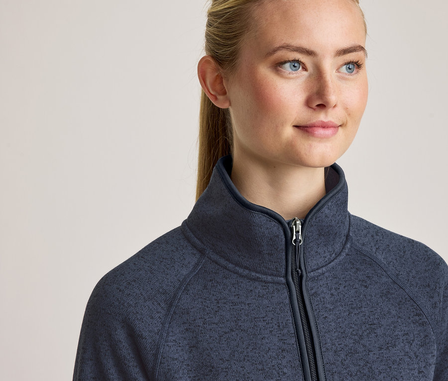 Gros plan d'une femme aux cheveux blonds et aux yeux bleus, portant une veste polaire bleu marine zippée avec un col montant.