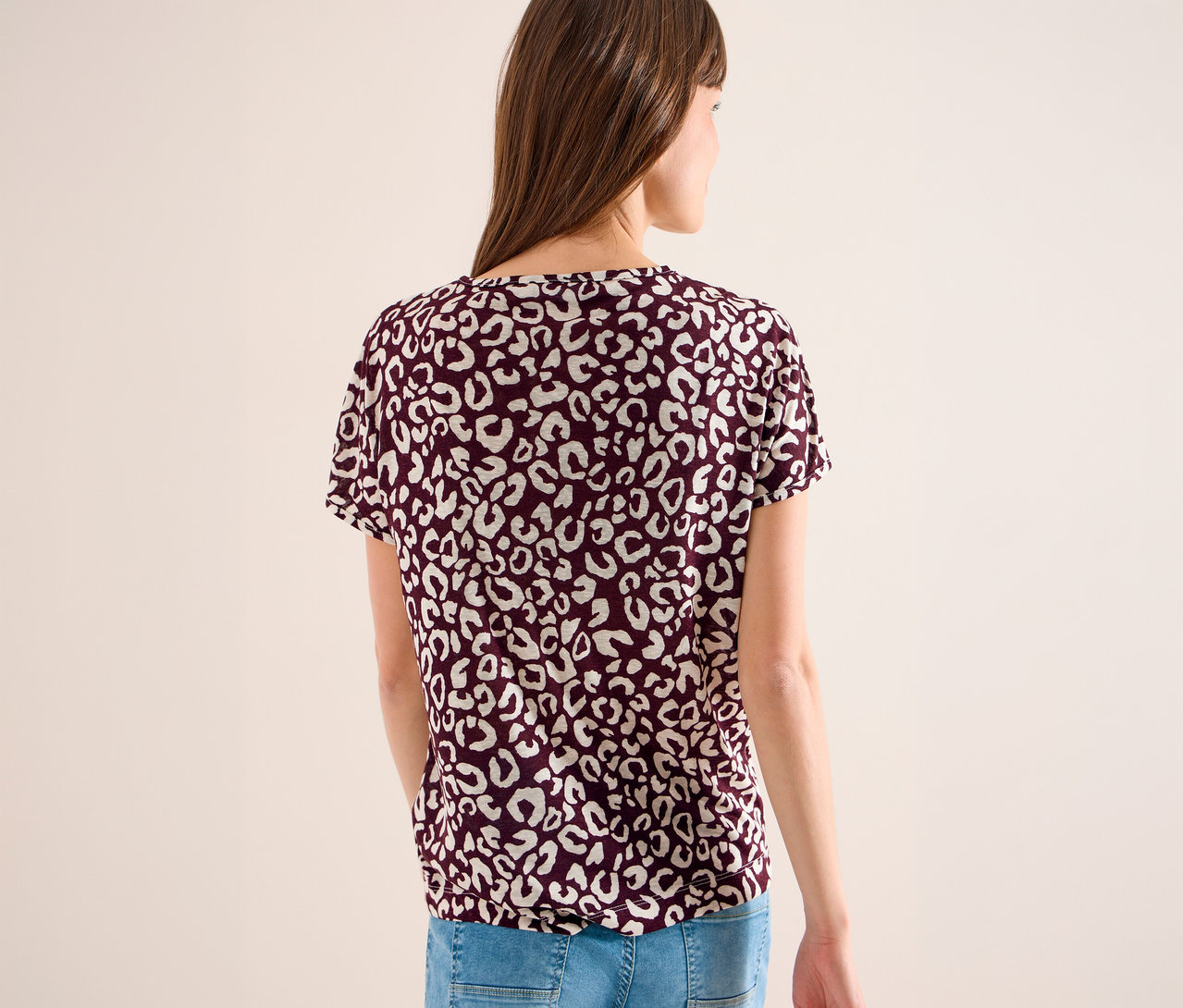 Femme vue de dos portant un t-shirt bordeaux à motif léopard blanc et un jean bleu.