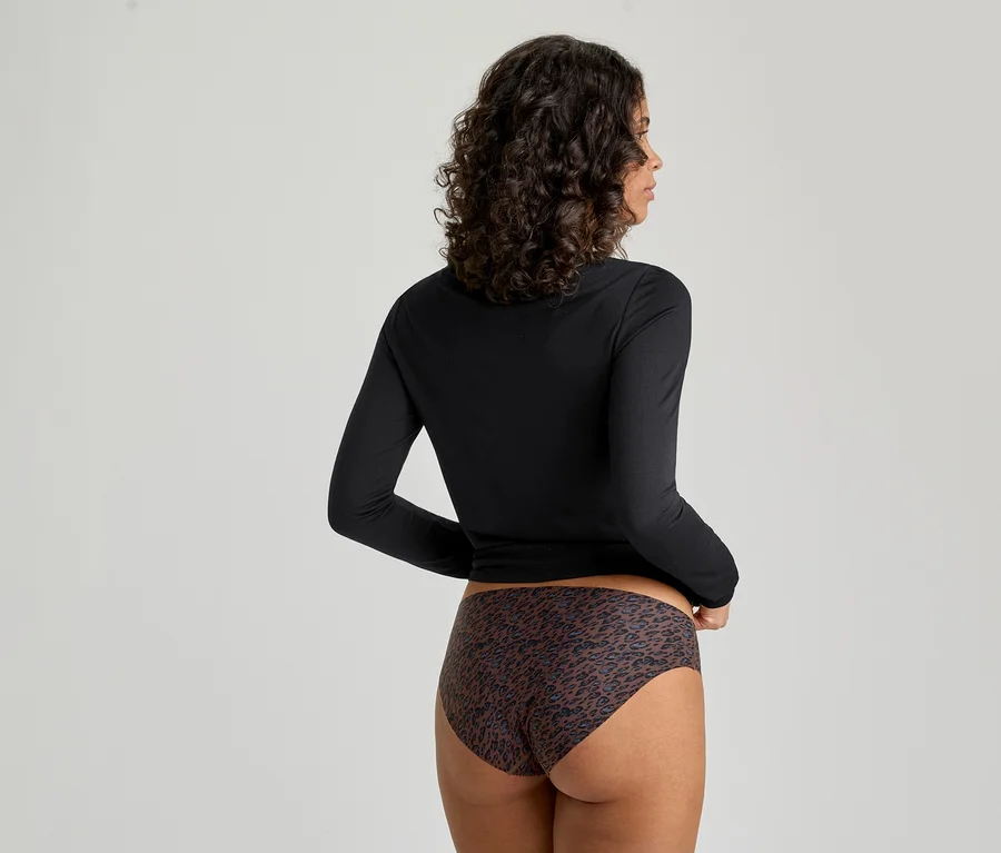 Une femme vue de dos, portant un haut noir à manches longues et une culotte marron à imprimé léopard. Elle a les cheveux foncés et bouclés et est légèrement tournée vers sa droite.