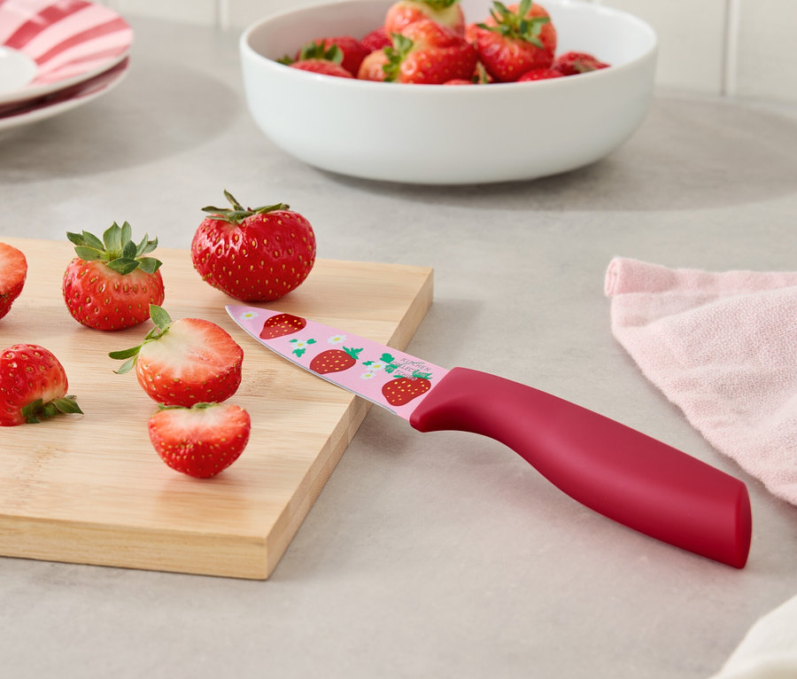 Des fraises et un couteau à motifs de fraises sur une planche à découper.