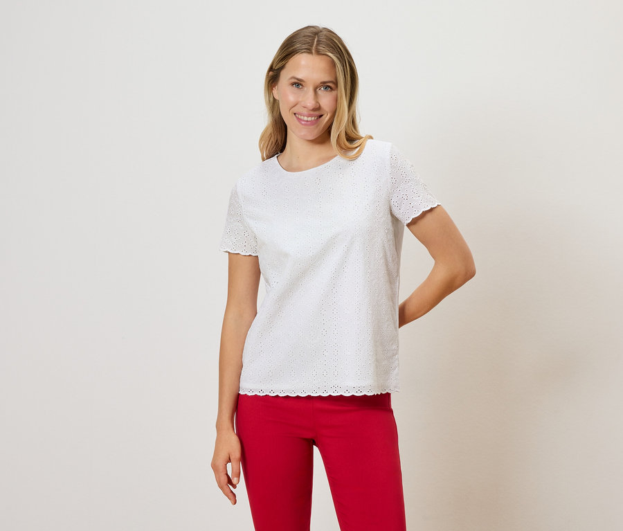 Femme blonde portant un t-shirt blanc en broderie anglaise et un pantalon rouge.