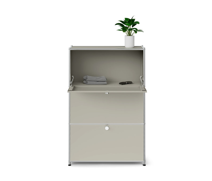 Armoire modulaire gris clair avec cadre chromé, section supérieure ouverte contenant des articles gris pliés et des lunettes de soleil, tiroir inférieur fermé et plante verte dans un pot blanc sur le dessus.