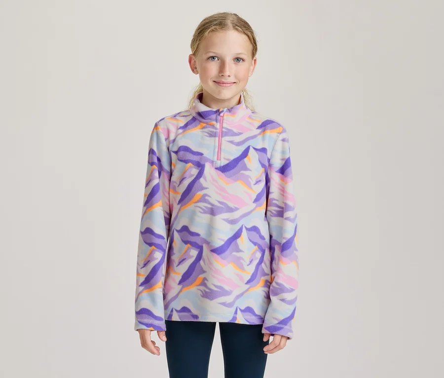 Jeune fille souriante portant un haut en polaire à manches longues avec un motif abstrait coloré dans des tons de violet, bleu, rose et orange, et un col zippé rose.