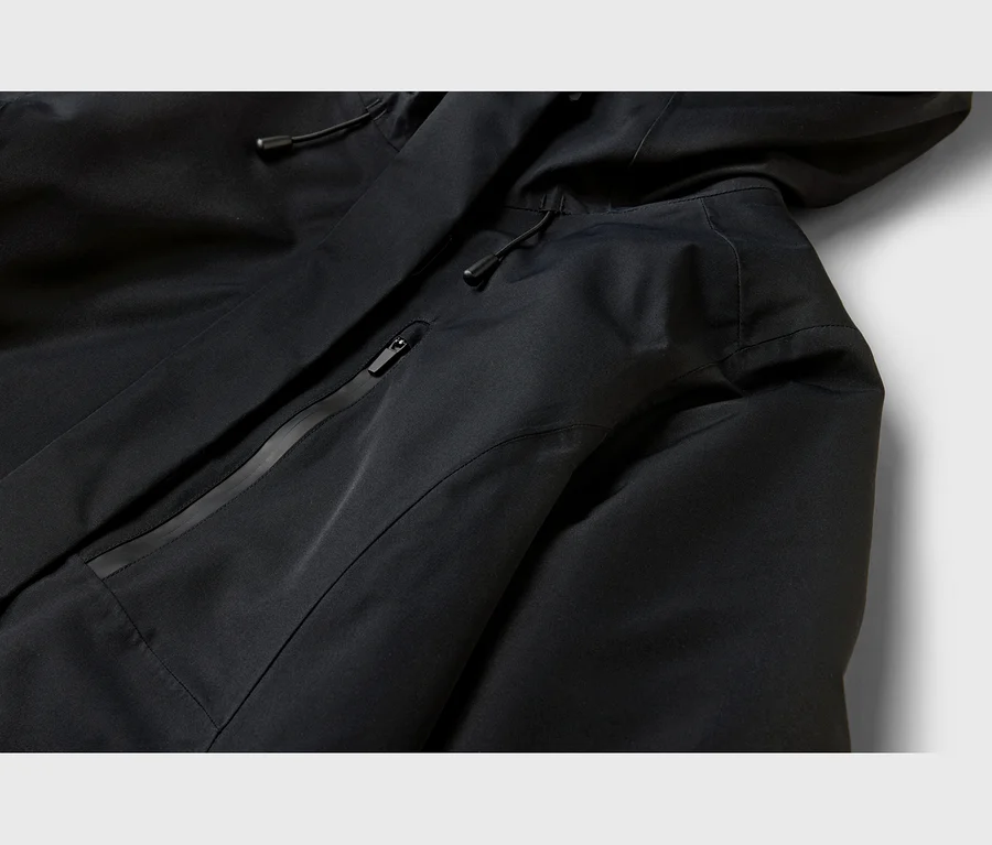Gros plan d'une veste technique noire à capuche, avec une poche zippée diagonale scellée et des cordons de serrage.