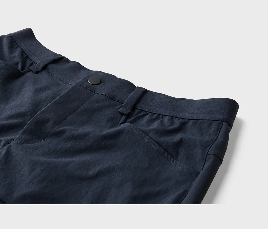 Pantalon bleu foncé, gros plan sur la taille avec un bouton noir, des passants de ceinture et une poche avant.