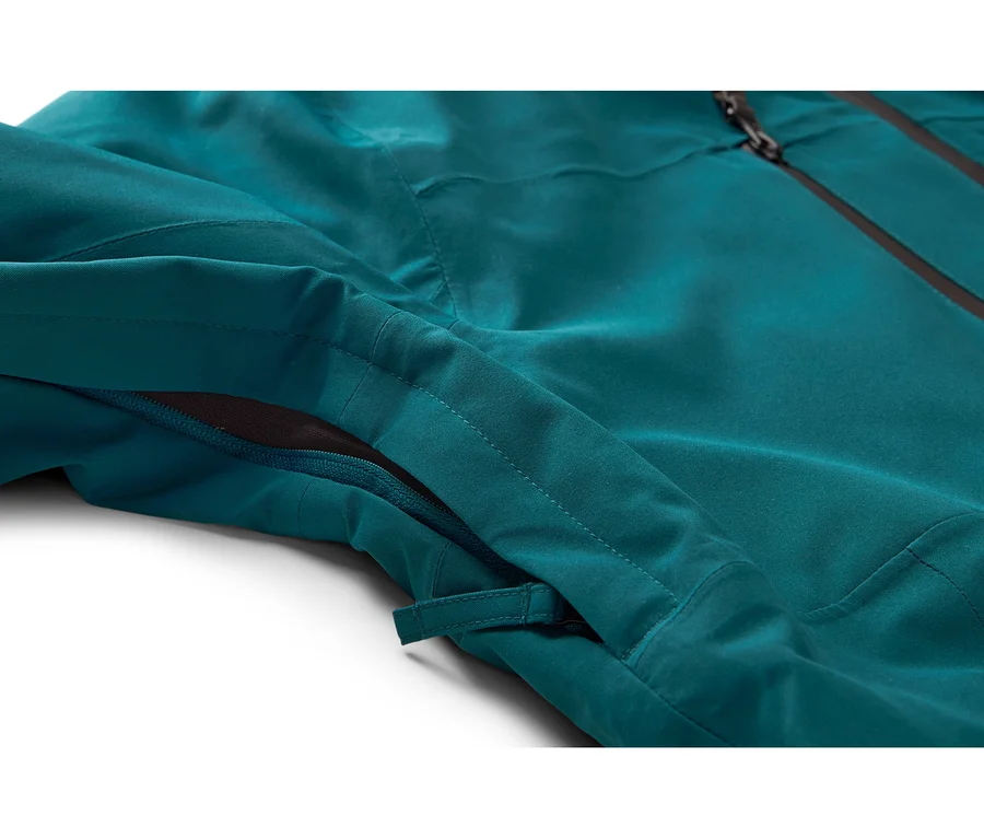 Gros plan d'une veste sarcelle avec une fermeture éclair latérale partiellement ouverte révélant une maille foncée, et une fermeture éclair principale noire visible en haut.