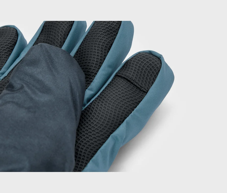 Gros plan d'un gant bleu foncé et sarcelle, montrant la paume avec un matériau de préhension texturé noir sur le bout des doigts et la paume, et un tissu lisse sur le dos.