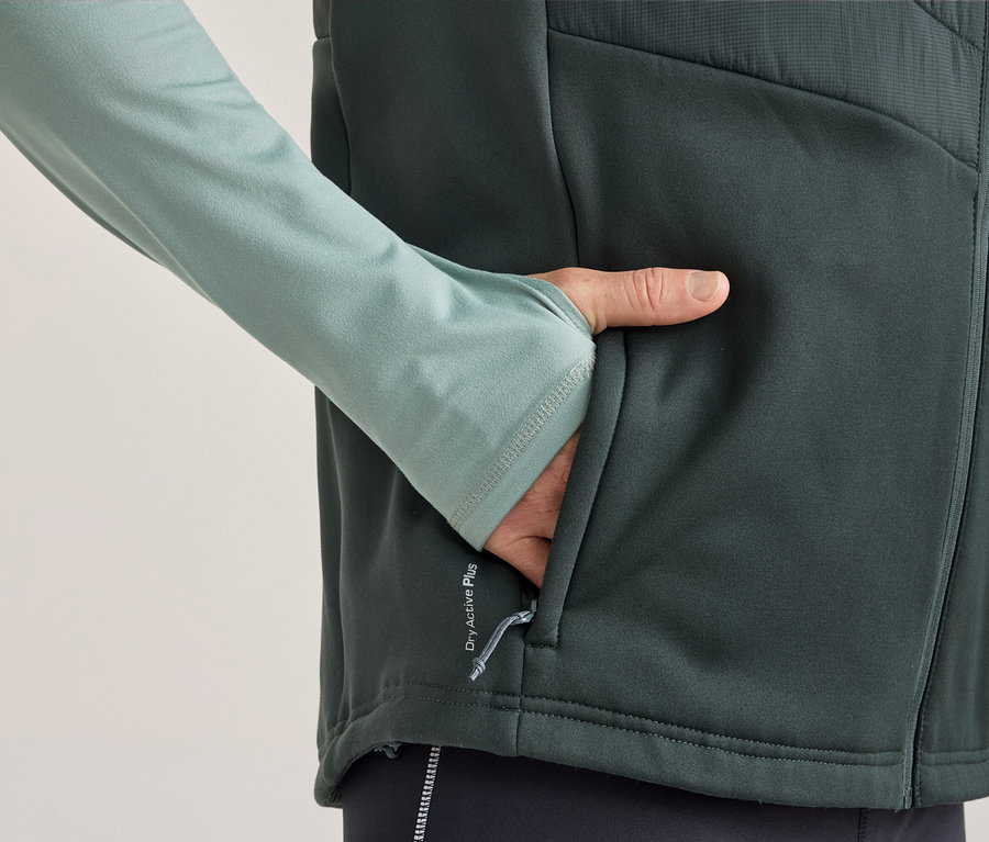 Personne portant un haut à manches longues vert clair avec des passe-pouces et un gilet gris foncé, la main dans la poche du gilet. Le gilet porte l'inscription « Dry Active Plus ».