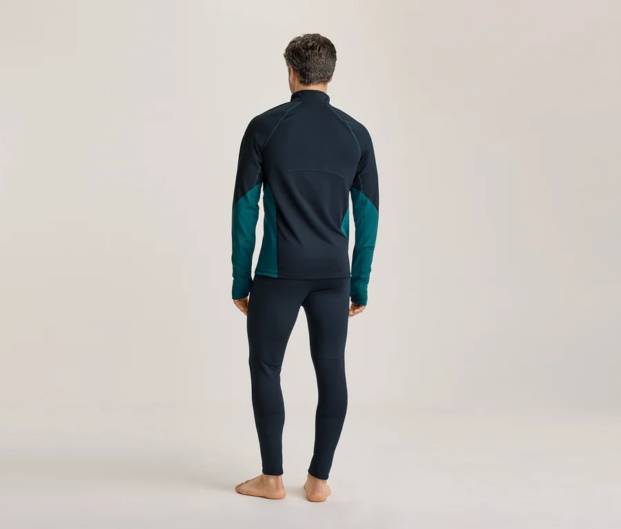 Homme vu de dos, portant un haut à manches longues bleu foncé et sarcelle et un legging bleu foncé, debout pieds nus.