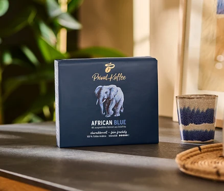 Un paquet de Privat Kaffee African Blue – 500 g moulu est posé sur une table à côté d'une tasse et d'un pichet.