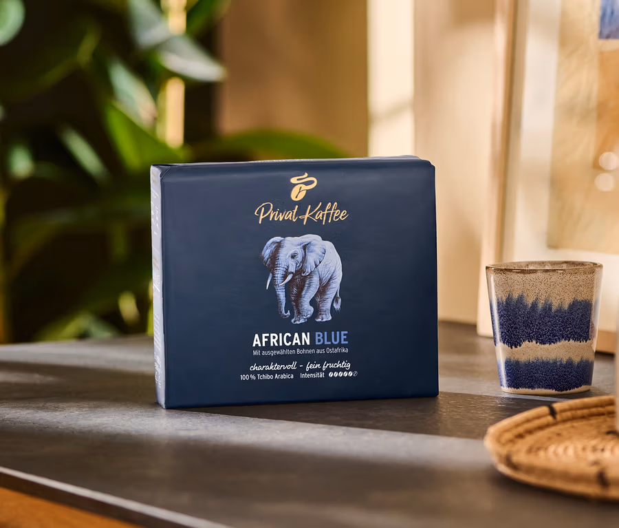 Un paquet de Privat Kaffee African Blue – 500 g moulu est posé sur une table à côté d'une tasse et d'un pichet.