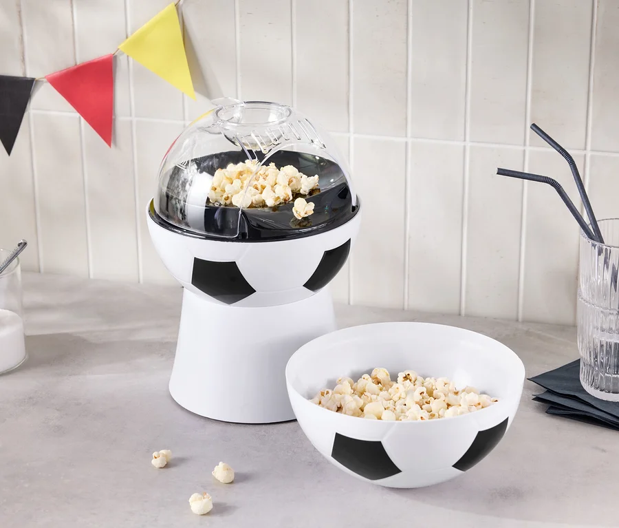 Une machine à pop-corn en forme de ballon de football se trouve à côté d'un bol de pop-corn et d'un verre avec des pailles.