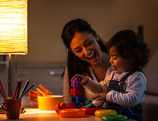 Faites confiance aux produits Tchibo : une femme est assise sur le canapé avec son bébé sur ses genoux pendant qu'elle parle au téléphone et examine un grande feuille – à côté d'elle se trouve son ordinateur portable.