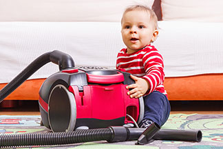 Un enfant portant un pull rayé rouge et blanc s'assoit par terre à côté d'un aspirateur rouge et noir.