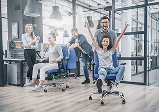 Cinq jeunes collègues s'amusent à rouler avec leurs chaises de bureau.