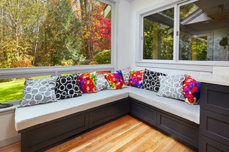 Se mettre tout simplement à l'aise : un banc d'angle confortable dans le salon devant une fenêtre, décoré avec des nombreux coussins colorés.