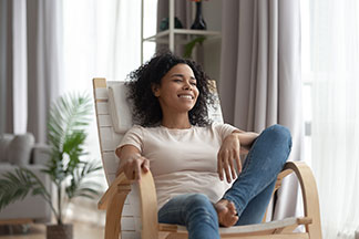Détente grâce à une bonne qualité : une jeune femme est assise, détendue, dans son fauteuil en bois aux accoudoirs courbés.