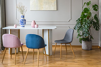 Forme élégante : sur une table blanche rectangulaire se trouvent trois chaises à manger en forme de coques sans accoudoirs, de couleur rose, bleue et grise.