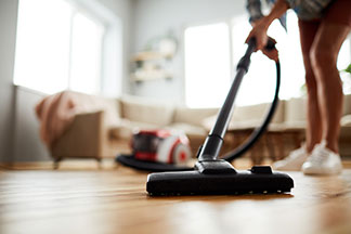 Une femme nettoie son plancher en bois dans le salon avec un aspirateur. La tête de l'aspirateur est visible en gros plan.