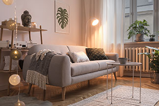 Ambiance chaleureuse grâce à l'éclairage du salon : un canapé gris dans un salon, devant lui une table ronde en métal sur un tapis rayé, derrière lui un petit lampadaire.