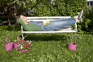 Banc pour l'extérieur : une femme est allongée, détendue, sur un banc blanc dans le jardin après avoir jardiné.