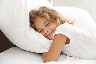 Une bonne qualité pour une bonne nuit de sommeil : une petite fille s'allonge sur le ventre dans son lit recouvert de blanc et se blottit dans son oreiller.