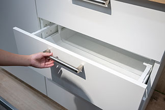 Une main de femme ouvre le tiroir d'une armoire de bureau blanche.