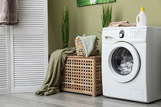 Le bon entretien des taies d'oreiller : un lave-linge plein se trouve à côté d'un panier à linge en bois dans la salle de bains.
