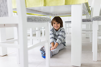 La qualité grâce au label TCM : un enfant souriant, aux cheveux bruns, est assis sous une table blanche entourée de chaises blanches.