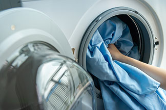 Le bon entretien des draps de lit : une main de femme met un drap de lit bleu dans un lave-linge.