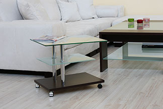 Chez Tchibo, vous achetez des tables d'appoint de haute qualité : un salon avec un canapé blanc et une table d'appoint rectangulaire en verre sur roulettes.
