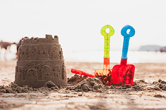 Amusez-vous avec des jouets d'extérieur : un château de sable sur la plage à côté duquel deux petites pelles en plastique sont enfoncées dans le sable.