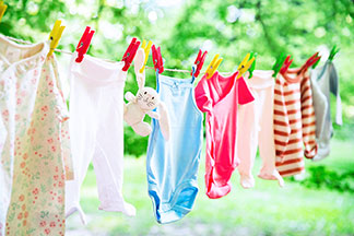 Une corde à linge est suspendue à l'extérieur – des vêtements de bébé y sont attachés avec des pinces à linge rouges, jaunes et vertes.